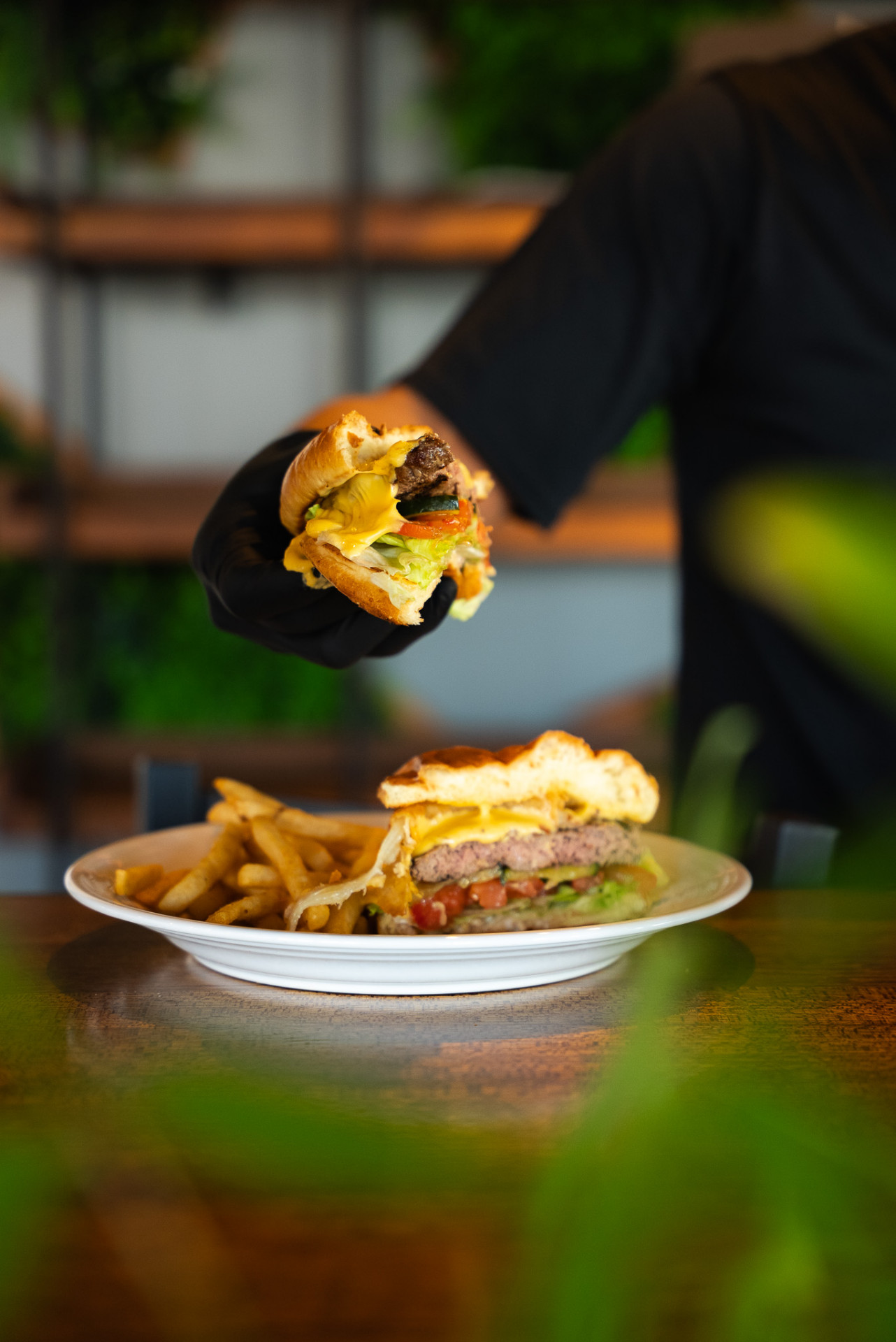 A chef in black gloves presenting a fresh Urban Kitchen burger with fries