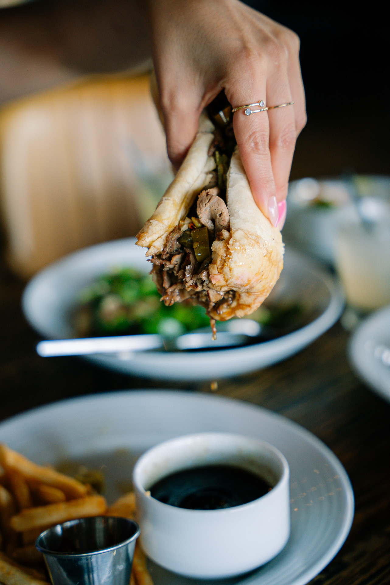 A hand holding a French dip sandwich with shaved beef over a bowl of au jus